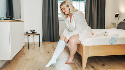 Venen Engel: Frau sitzt auf Bett und zieht sich Kompressionssocken an
