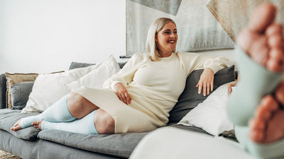 Venen Engel: Frau in Kleid und Kompressionsstrümpfen lächelnd auf Sofa