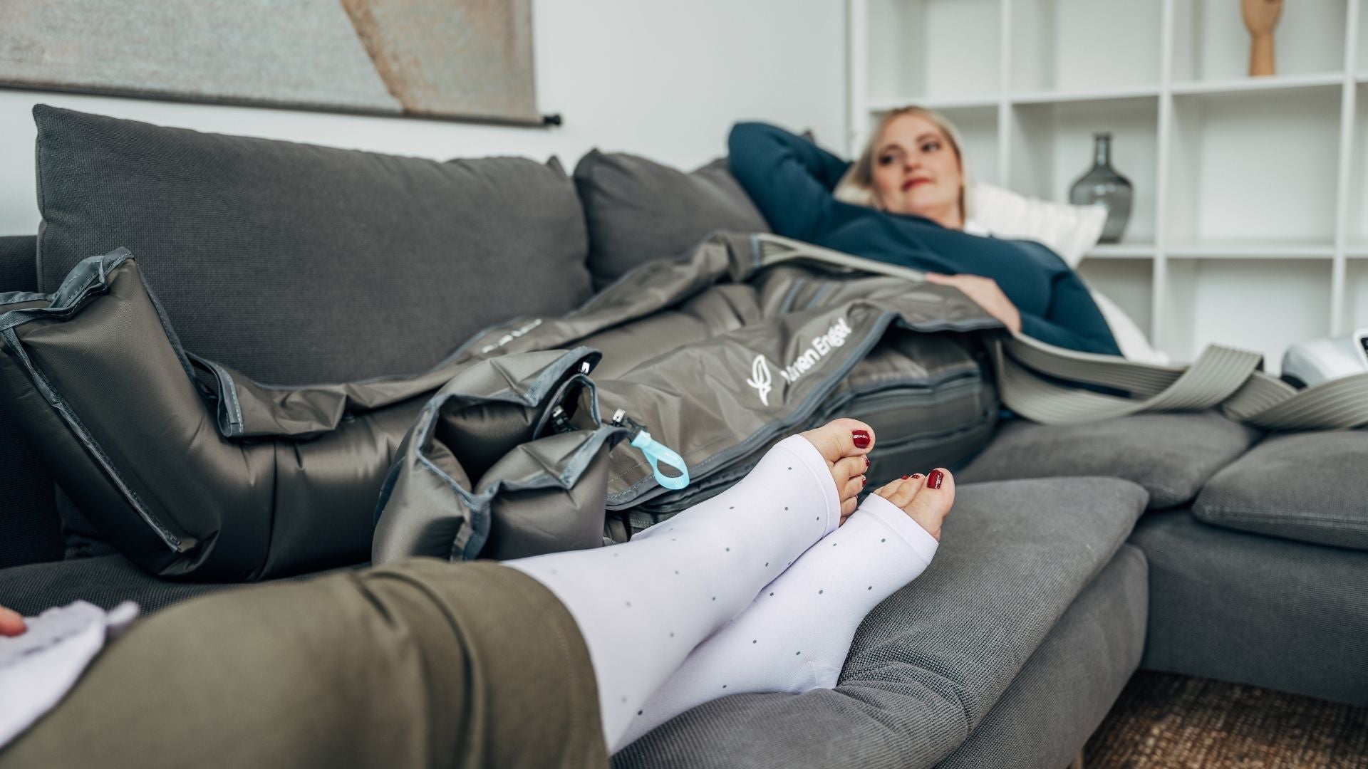 Venen Engel: Frau entspannt lächelnd auf Sofa mit Kompressionsmassagegerät