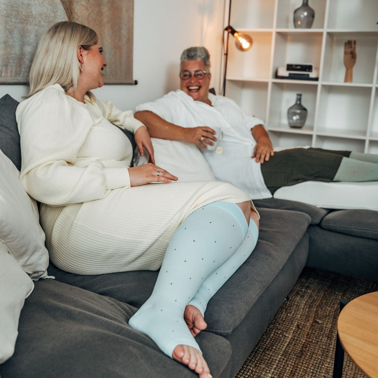 Venen Engel: 2 fröhliche Frauen auf Sofa mit Kompressionssocken