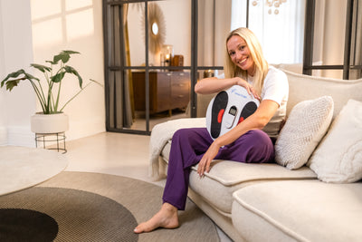 Venen Engel: Glückliche Frau auf Sofa mit EMS Venen Board im Schoß